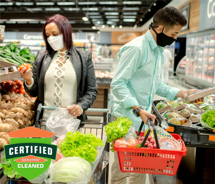Two adults shopping the produce section of a grocery store with masks on. Green Certified: SERVPRO Cleaned logo in bottom