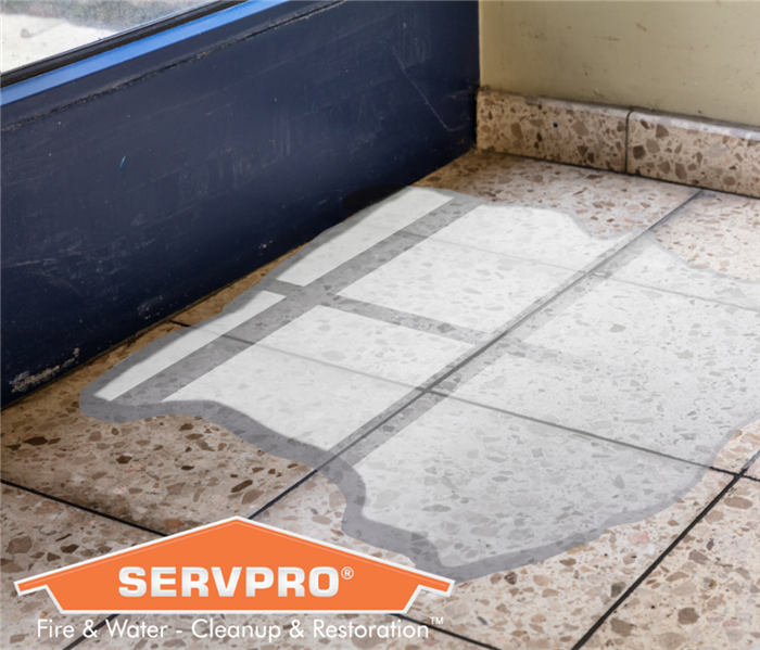 Water leaking into a puddle onto a brown tile floor. Orange SERVPRO logo in lower left hand corner.