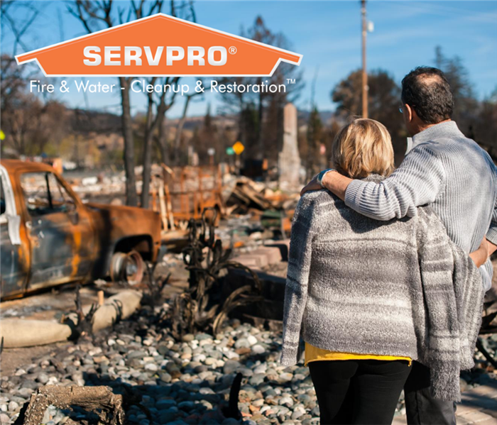 Man and woman standing facing away from the camera while looking at a destroyed area where there used to be a home